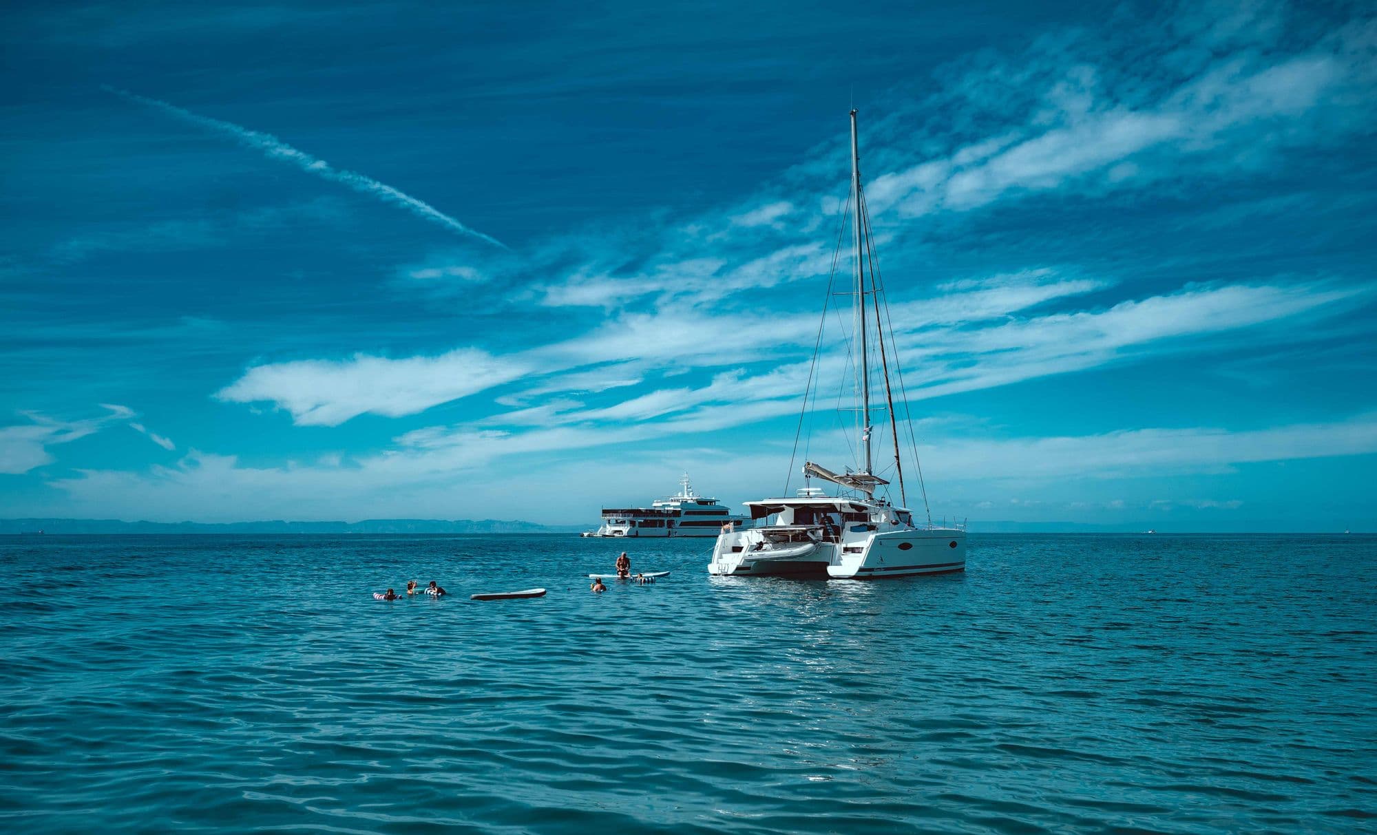 Catamaran at anchor in open water, guests swimming and paddleboarding alongside