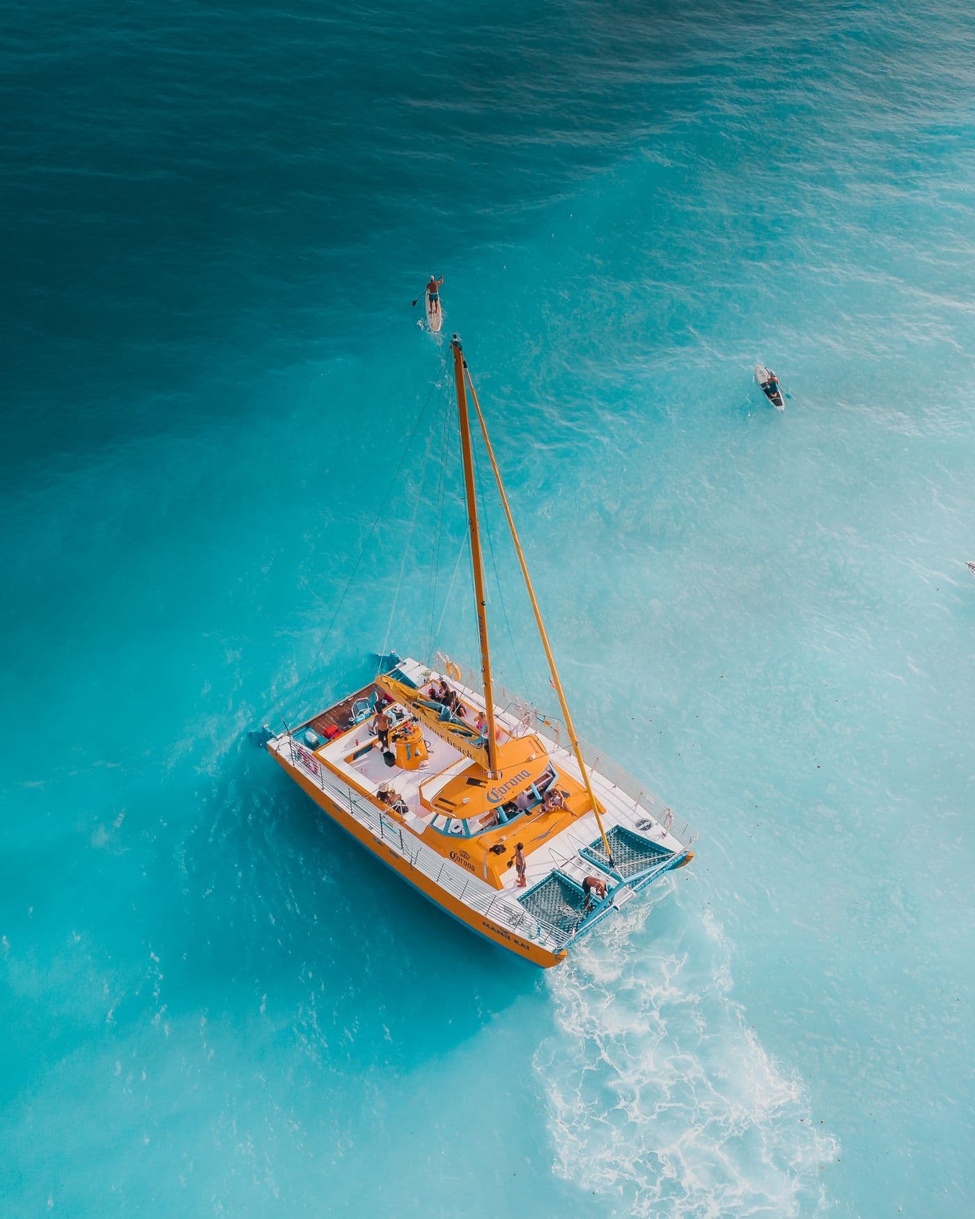 Catamaran seen from above at anchor, with guests paddleboarding on turquoise water