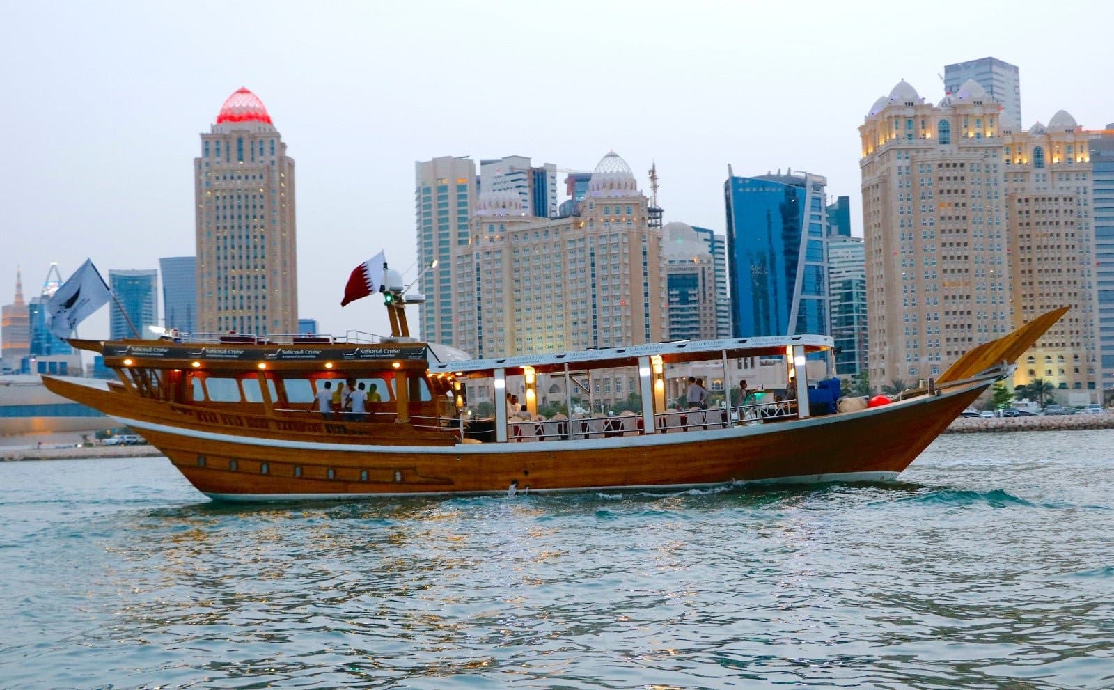 Sunset over the Doha skyline seen from the Corniche, with traditional boats on calm water